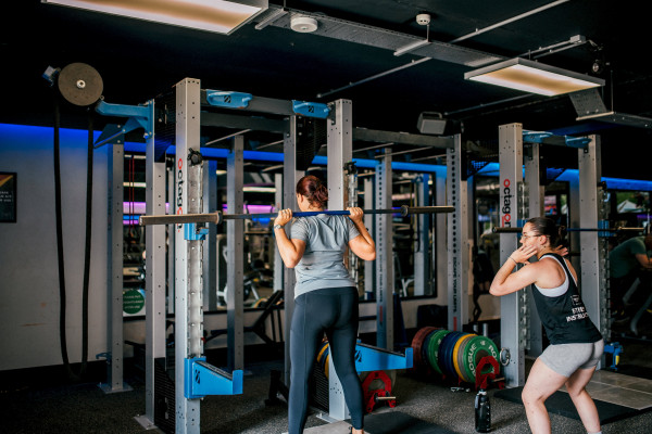 Female Health Club Instructor showing a female gym member how to load a barbell onto her shoulders