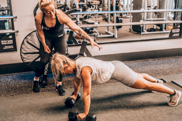Female instructor guiding female class member through pushups