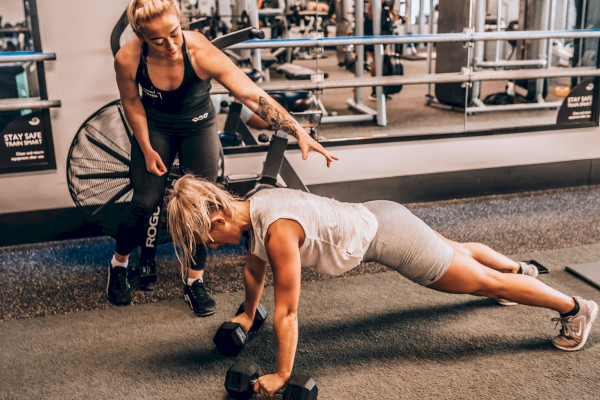 Female instructor guiding female class member through pushups