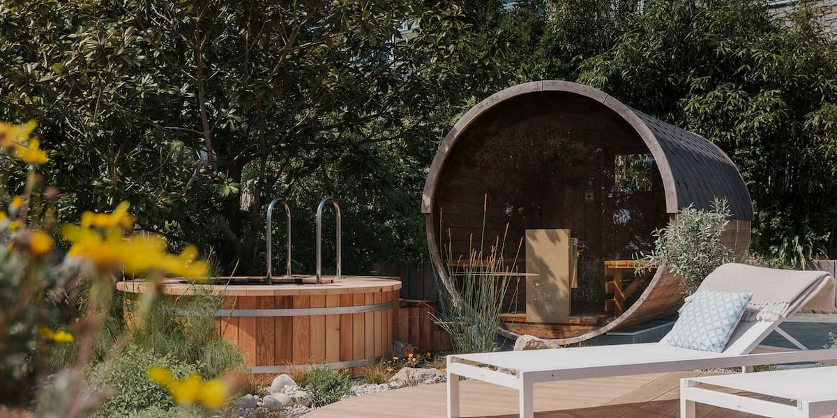 Outdoor spa patio with an outside wicker sauna , deckchair, hot tub and leafy trees creating a peaceful atmosphere.